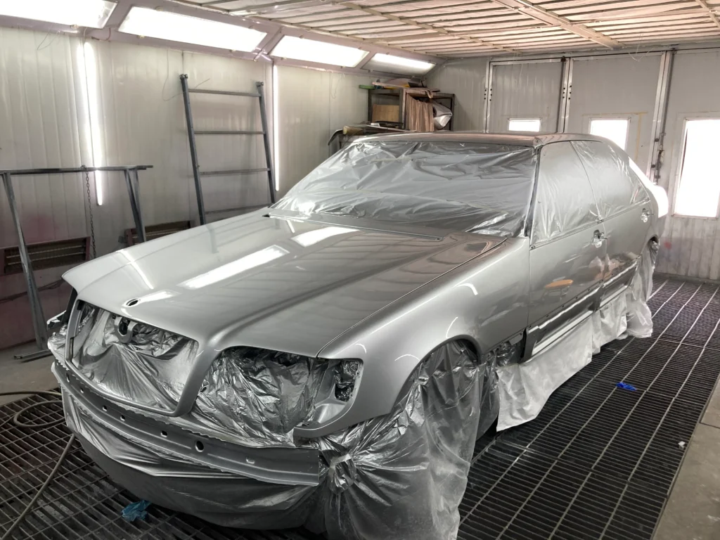 Silver car in a paint booth covered with protective plastic for masking, awaiting finishing touches or drying