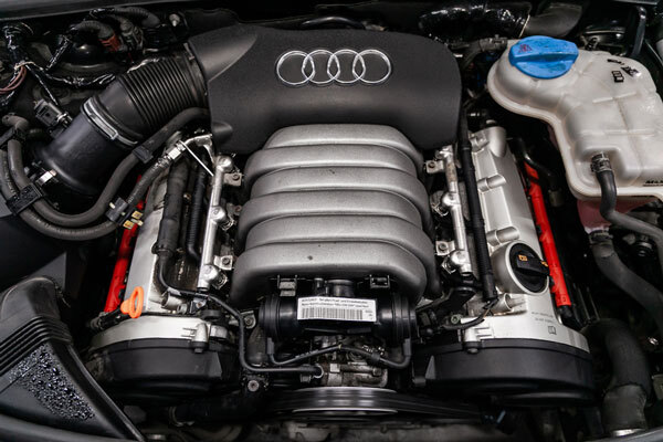 Under-hood view of an Audi engine with a ribbed silver intake manifold and the Audi logo on the engine cover.
