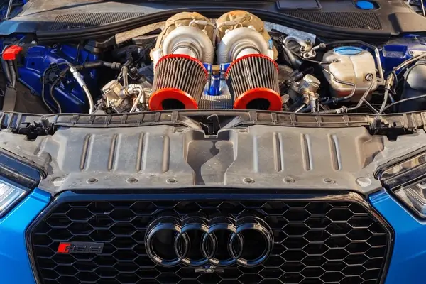 Front view of a blue Audi with hood open, showing twin turbo air intake filters and engine bay components under the hood.
