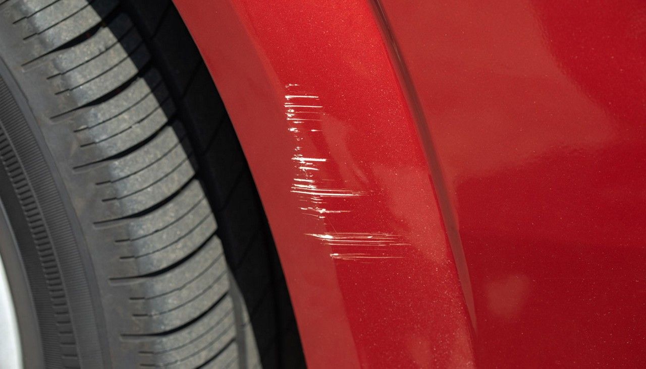 Red car fender with several white cosmetic scratches next to the tire area near the wheel well.