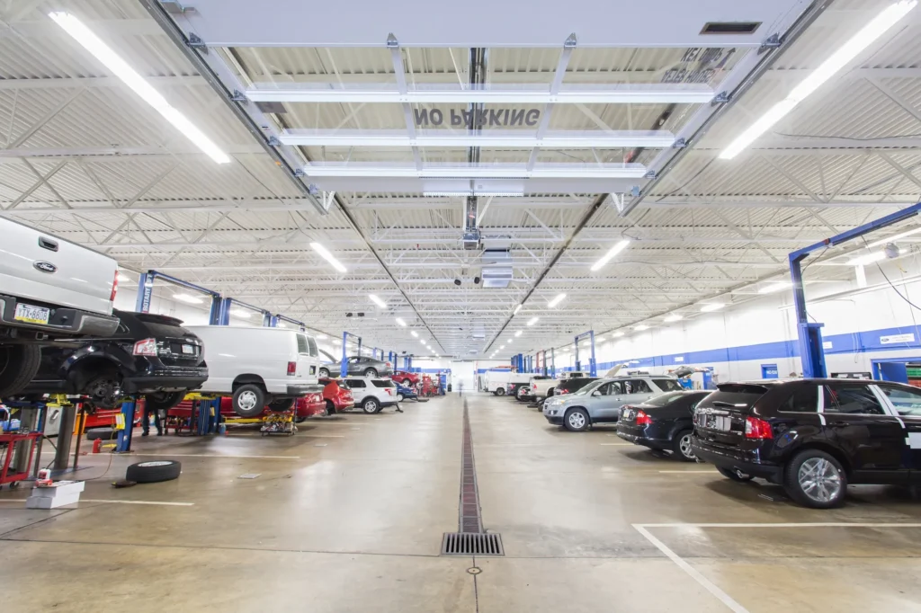 Wide view of an automotive repair shop with cars on lifts along both sides and a central aisle under bright lights.