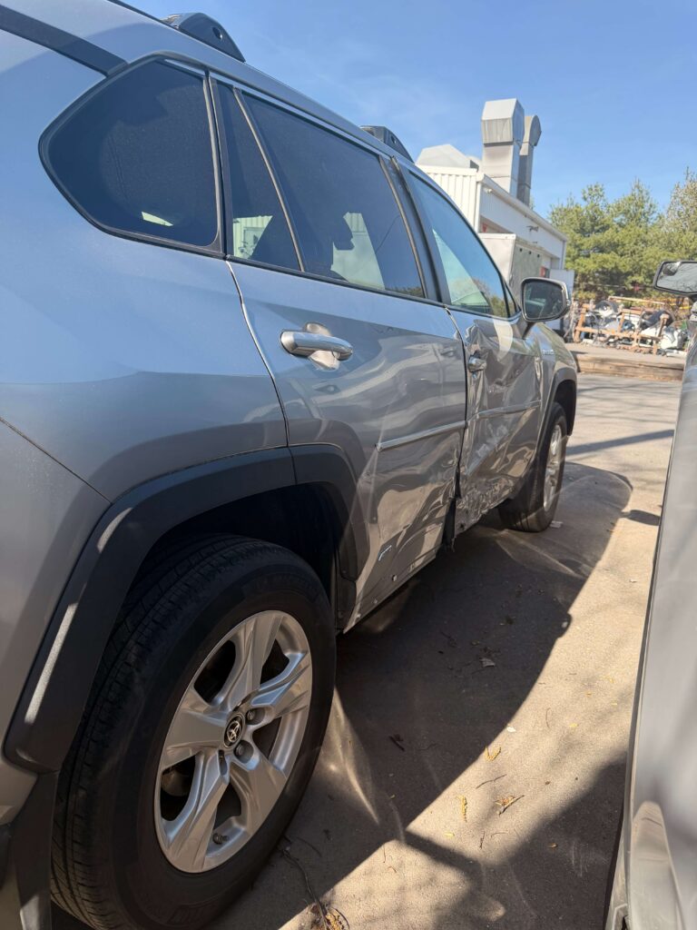 Blue SUV parked outdoors with noticeable dent along the rear passenger door panel on the driver's side window line, wheel visible in foreground.