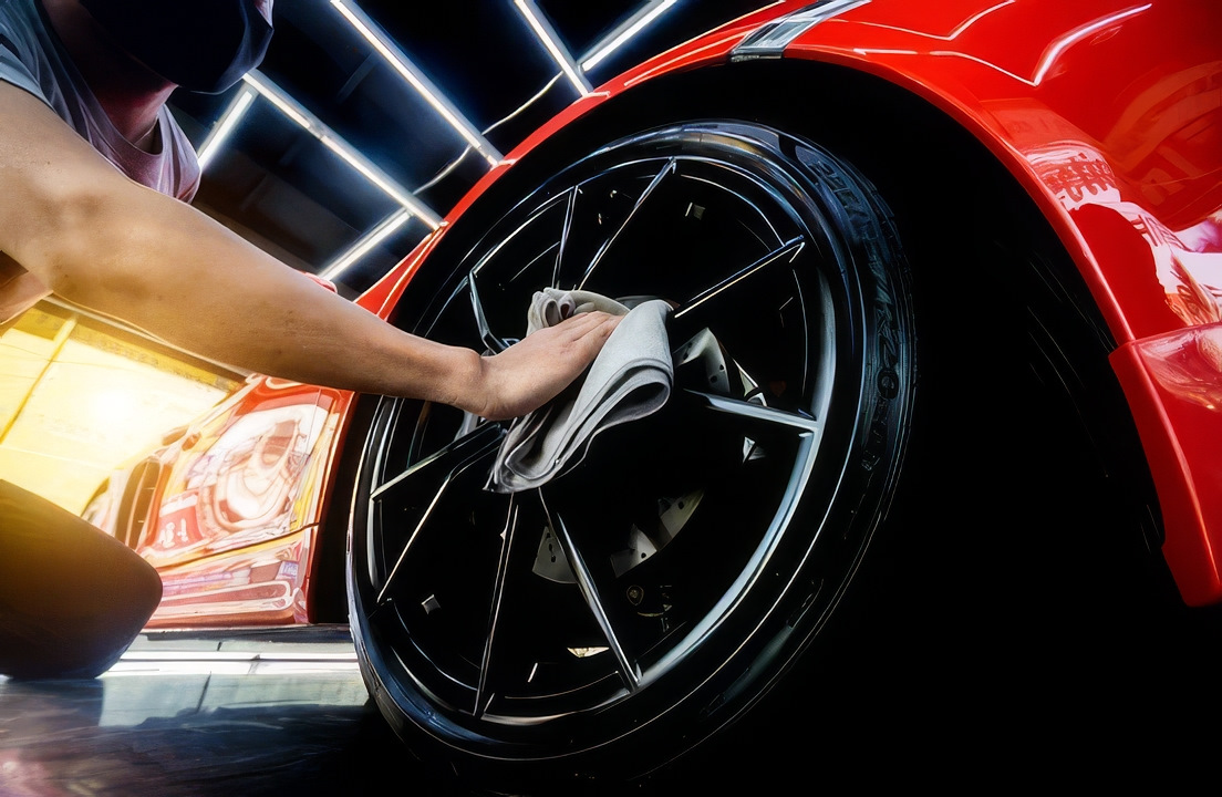 Person wiping a black alloy wheel of a red sports car with a cloth.