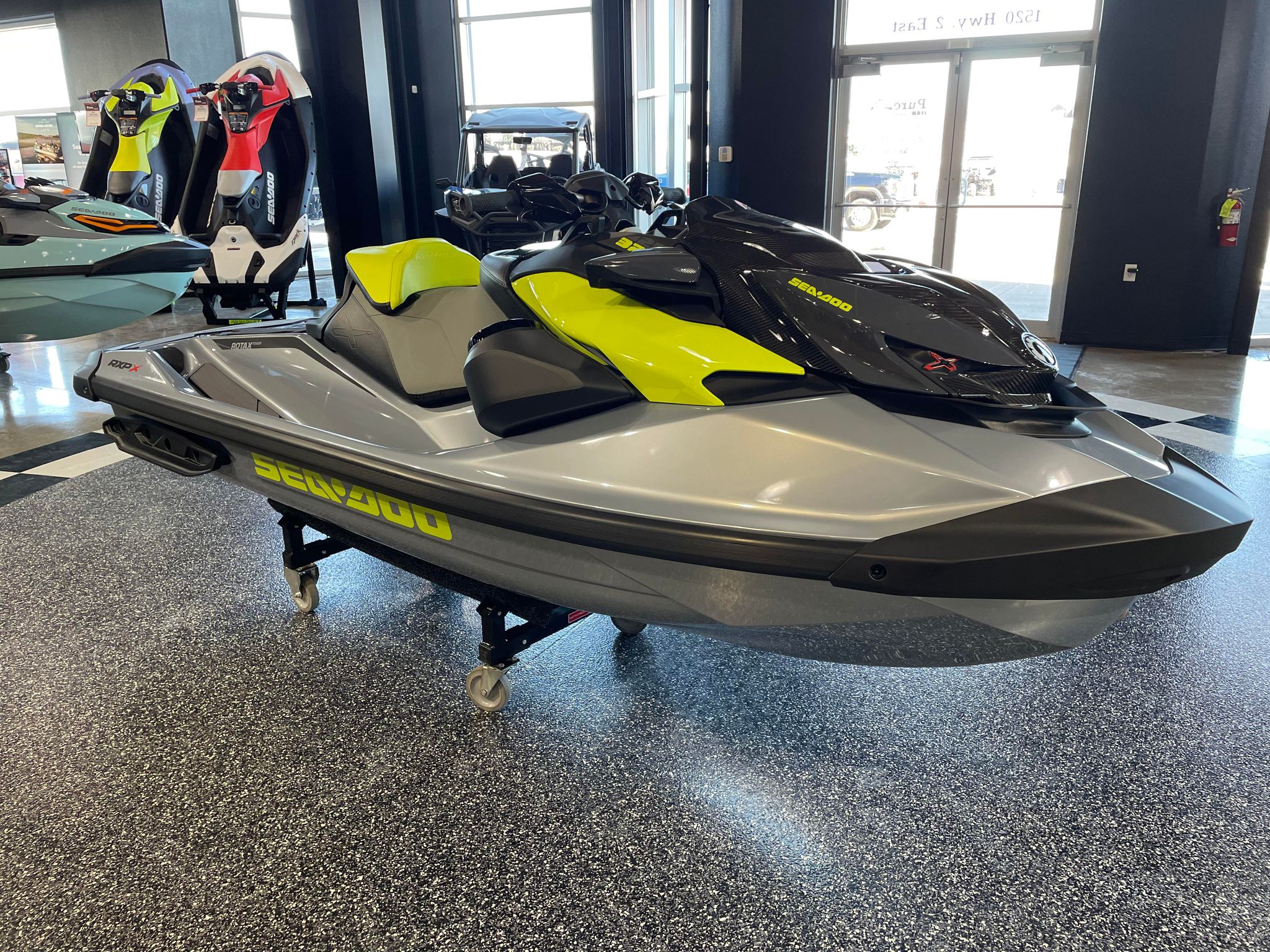 Inside showroom with a yellow-and-gray Sea-Doo jet ski in the foreground and colorful watercraft behind it.