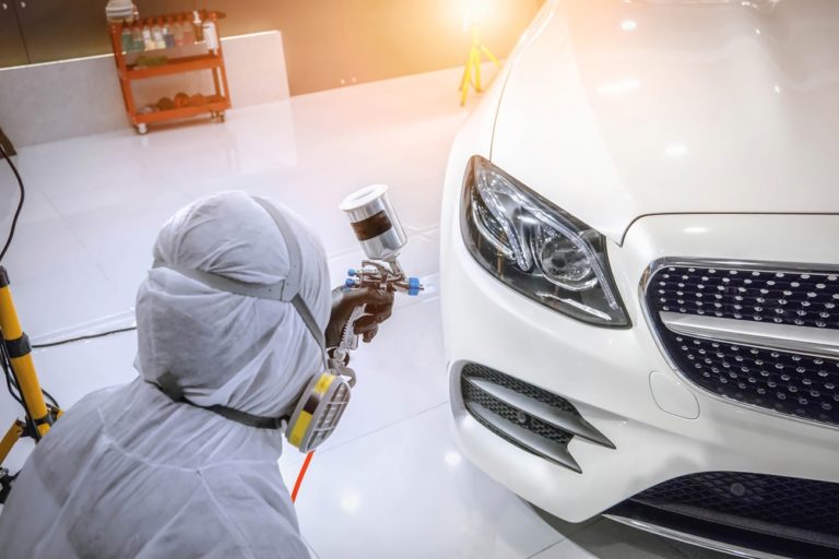 Painter in protective suit and respirator spraying a white car in a bright workshop?