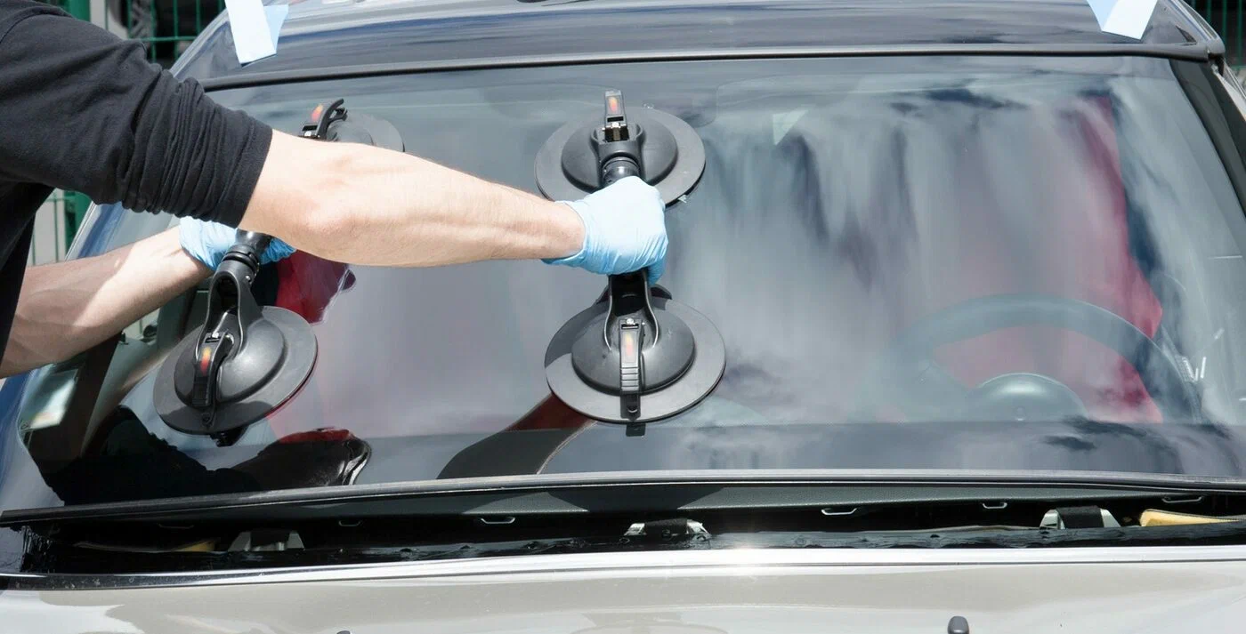 Tech with blue gloves attaching suction cups to a car windshield.