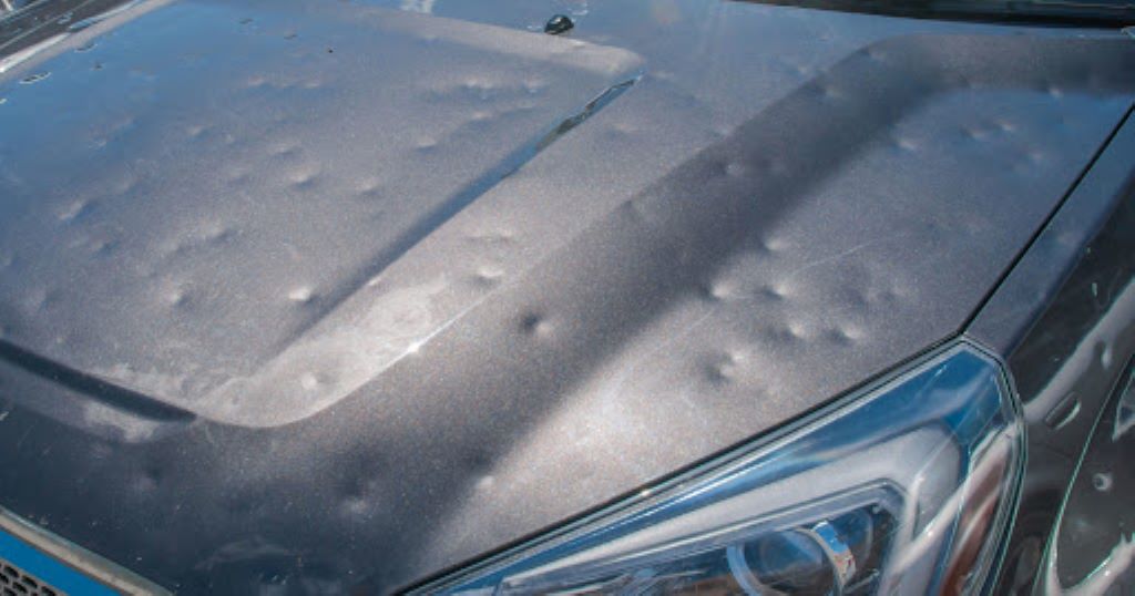 Close-up of a car hood and headlight showing numerous dents from hail damage.