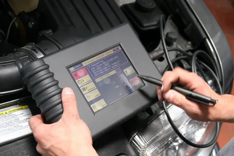 Automotive technician using a handheld diagnostic scanner under the hood, screen displaying diagnostics.
