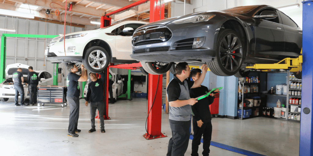 Mechanics inspect a dark gray car raised on a hydraulic lift in a bright auto repair shop for service.