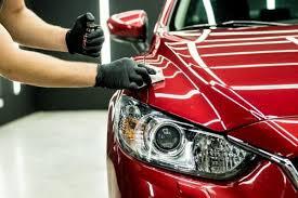 Close-up of a person in gloves polishing a shiny red car, focusing on the hood and headlight.