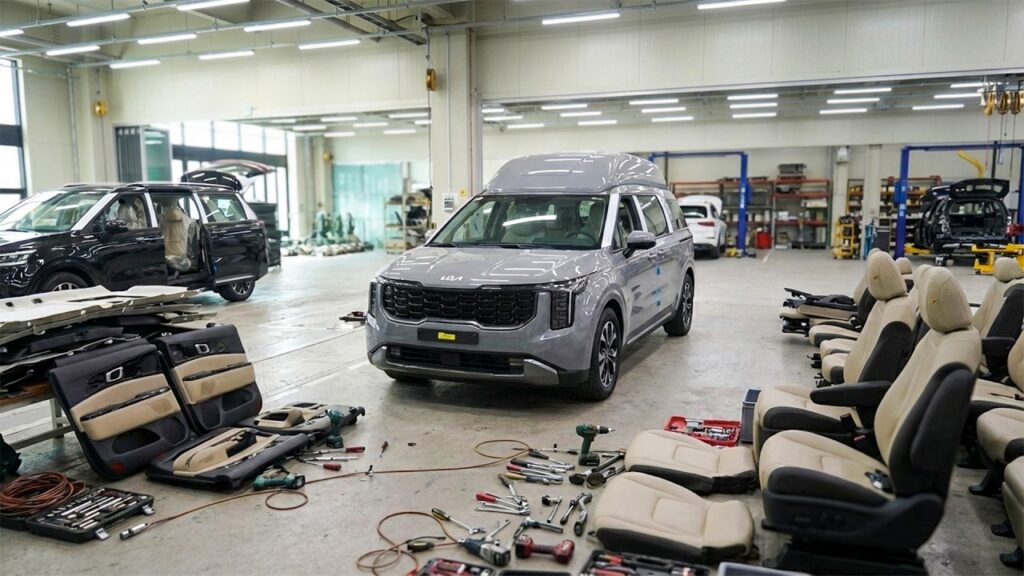 Inside a car workshop with a gray SUV in the center and many car seats and tools laid out on the floor around it.