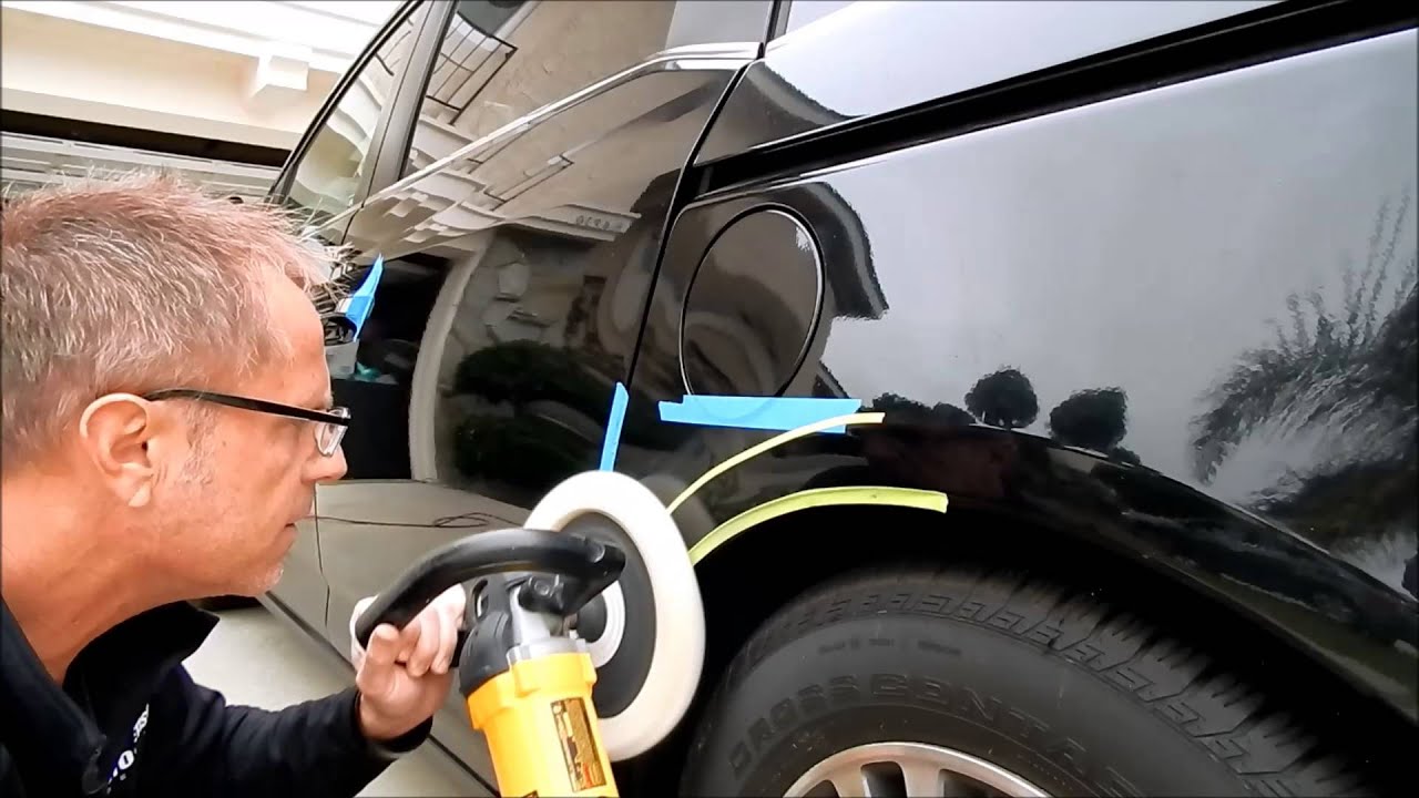 Man polishing a dark car door with a rotary buffer, blue painter's tape guides nearby, tire visible in the foreground.